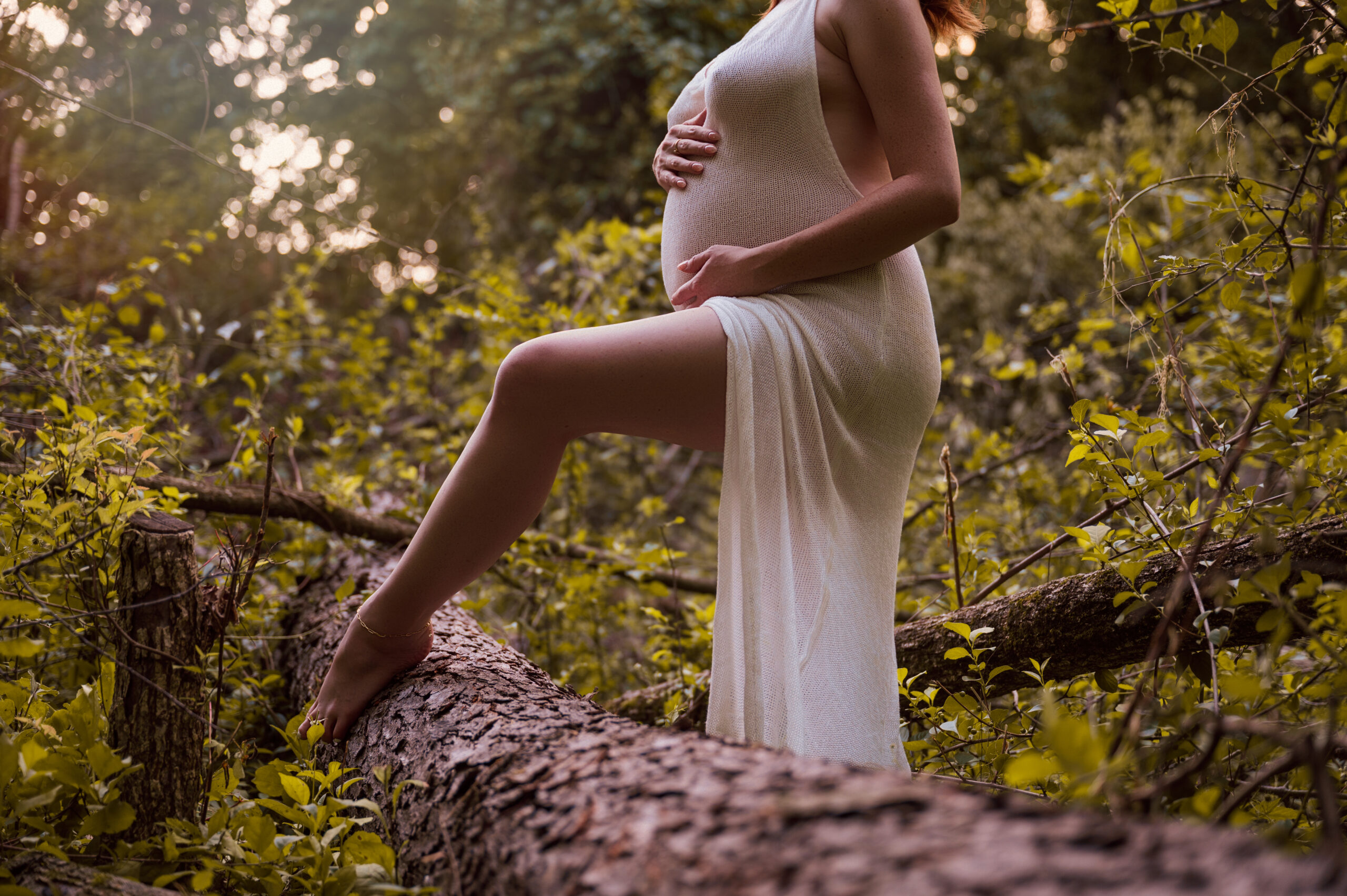 woman draped in white dress posing with a ballerina toe on log